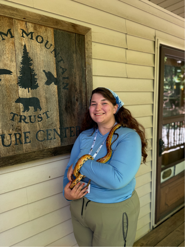 Megan holds a cornsnake in front of the Balsam Mountain Trust sign